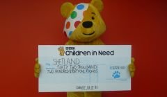 The Children in Need mascot Pudsey Bear handing over more than £62,000 to charities in Shetland - Photo: BBC