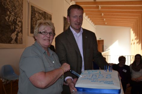 Andrina Tulloch, who helped set up SBSS, cutting a cake to mark the service's seventh birthday as MSP Tavish Scott looks on. Photo: Shetnews