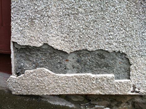 Crumbling concrete blocks beneath cracked harling, with iron ore particles visible. Photo Shetnews