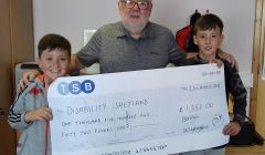 Benji and Dougray Bain presenting a cheque for £1,552 to Disability Shetland vice-chairman George McGhee.