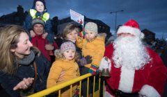 Santa claus with a group of children in front of a fence.