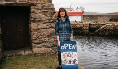 A woman standing next to a sign that says open.