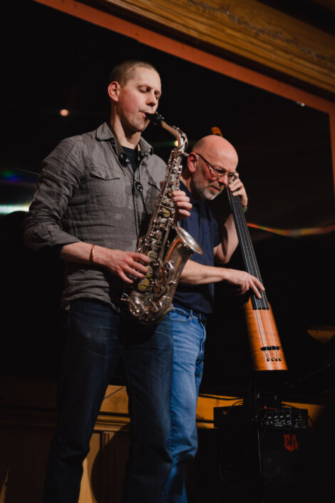 Two musicians perform on stage; one plays a saxophone while the other plays an upright bass.