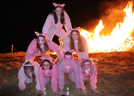 A group of people wearing pink costumes with bunny ears are forming a human pyramid in front of a large bonfire at night.