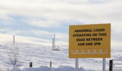 Yellow sign on snow-covered landscape reads "Abnormal loads operating on this road between 6am and 3pm.