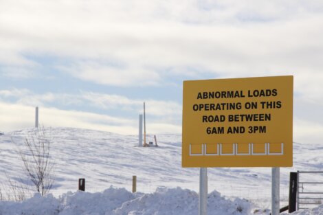 Yellow sign on snow-covered landscape reads "Abnormal loads operating on this road between 6am and 3pm.