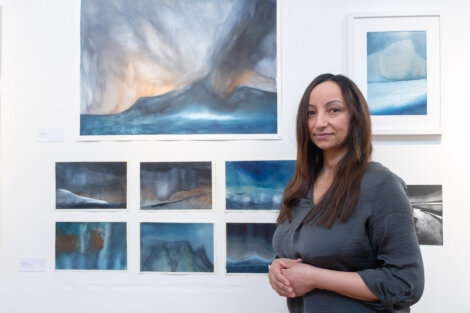 A person stands in front of an art exhibit featuring multiple abstract landscape paintings in a gallery.