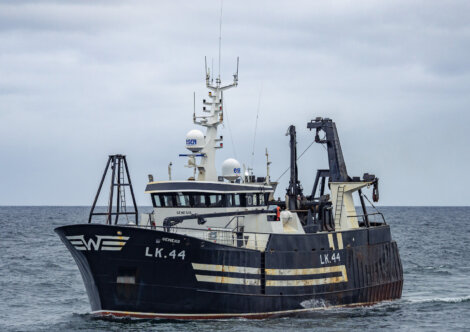 A deep-sea fishing vessel with the identification number LK 44, fitted with various antennas and equipment, sails on a calm sea under an overcast sky.