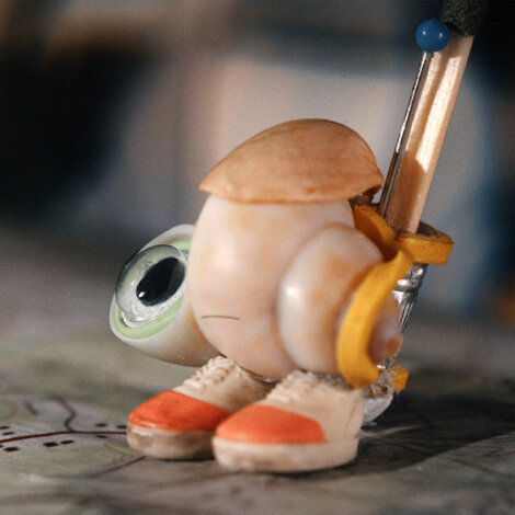 A small, anthropomorphic shell with a single eye, tiny shoes, and a pencil attached to its back stands on a surface.