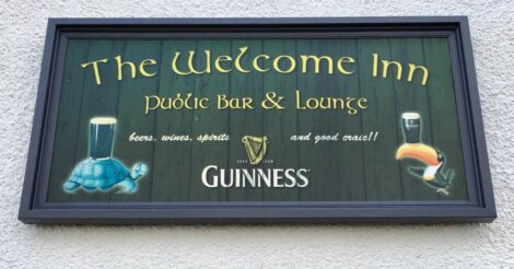 Sign for "The Welcome Inn" highlighting beer, wine, spirits, and "good craic," with Guinness branding, featuring illustrations of a turtle with beer and a toucan with beer.