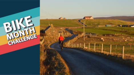 A person is cycling on a rural road at sunset. To the left, there is a graphic with the text "Bike Month Challenge" in colorful, bold letters.