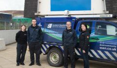 Four people standing next to a Scottish & Southern Electricity Networks utility vehicle. The vehicle is parked outside a building, and all individuals are dressed in work uniforms.