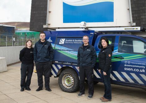 Four people standing next to a Scottish & Southern Electricity Networks utility vehicle. The vehicle is parked outside a building, and all individuals are dressed in work uniforms.