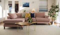 A living room with a pink sectional sofa adorned with pillows, a wooden coffee table, a potted plant, and wall art.