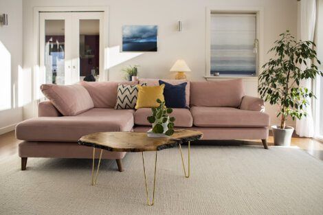 A living room with a pink sectional sofa adorned with pillows, a wooden coffee table, a potted plant, and wall art.