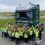 A large group of children and two adults, all wearing high-visibility vests, stand in front of a green truck labeled "NORTHWARDS" and "SHETLAND" in an outdoor area.