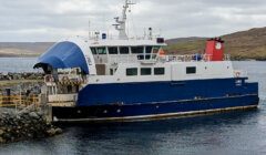 A blue and white ferry named "Linga" docks at a rocky pier in a calm coastal area under a cloudy sky.