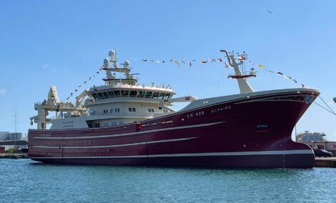 A large red and white fishing vessel, LK 429 Altaire, is docked in a port under a clear blue sky with signal flags decorating the entire length of the ship.