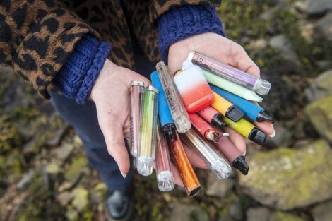 Person holding a collection of used disposable vapes in both hands, with a rocky background.