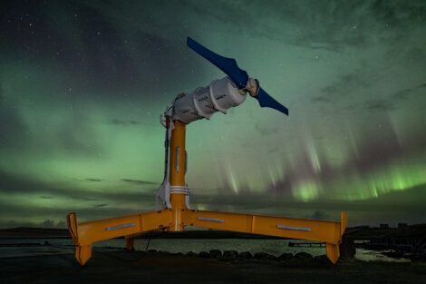 A tidal turbine stands against a backdrop of green aurora borealis in a dark night sky.