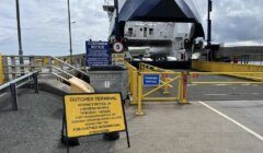 A ferry docked at Gutcher Terminal with a sign warning about upcoming linkspan works and alternative foot passenger arrangements. A passenger walkway and a customer notice are also visible.