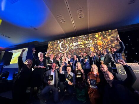 A group of people pose on stage holding awards at the Aquaculture Awards 2023 with a celebratory backdrop displaying the event name.