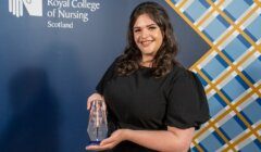 A person in a black dress holding an award stands in front of a backdrop that reads "Royal College of Nursing Scotland.