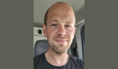 A man with a receding hairline and short beard is sitting in a vehicle, looking at the camera with a neutral expression.