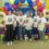 Six people wearing matching "25 years" t-shirts stand in front of a colorful balloon arch with the number 25.