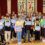 A group of children and an adult pose with certificates in front of a banner about road safety. Stained glass windows are in the background.