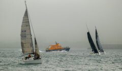 Three sailboats and an orange rescue boat navigate through foggy waters.