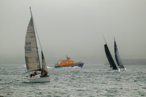 Three sailboats and an orange rescue boat navigate through foggy waters.