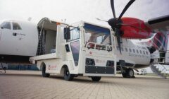 A runway utility vehicle is parked between two passenger airplanes, each branded with different airline logos. One of the planes has its rear door open and cargo being loaded or unloaded.