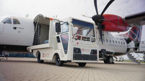 A runway utility vehicle is parked between two passenger airplanes, each branded with different airline logos. One of the planes has its rear door open and cargo being loaded or unloaded.