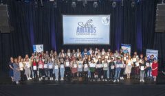 Group of people holding certificates on stage at the Saltire Awards Ceremony 2023, with a banner and screen displaying event information in the background.