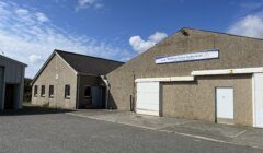 A concrete building with a sign reading "Shetland Global Seafood Ltd," featuring a large garage door and a smaller entrance, under a partly cloudy sky.