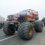 A red monster truck with large tires drives down a road during a parade with spectators on both sides.