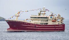 A large fishing vessel named Altaire LK 428 is sailing on the water, adorned with nautical flags and carrying lifeboats on its upper deck.