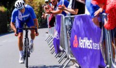 Cyclist in blue racing uphill past a cheering crowd behind barriers with NatWest branding.