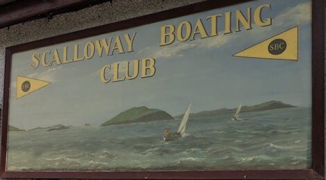 Signboard reading "SCALLOWAY BOATING CLUB" with sailing boats on the sea and islands in the background.