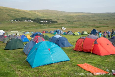 A field filled with colorful tents set up for camping, with rolling hills in the background and people gathered near the tents. © Austin Taylor Photography, 2013.