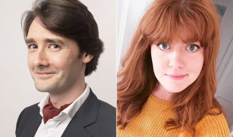 A man with brown hair in a suit and red scarf smirking on left; a woman with red hair in a mustard sweater smiling on right.