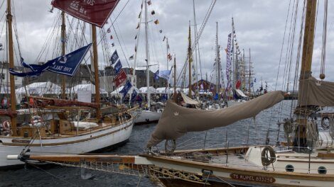 A row of boats with colorful flags docked at a marina during an event. Overcast sky in the background.