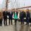 A group of eight people standing on a dock in front of a sailing ship on an overcast day. Seven are posing for the photo, and one appears to be walking slightly out of frame.