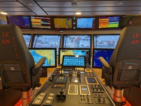 The image shows a ship's navigation bridge with multiple control panels, monitors displaying various navigational data, and two chairs labeled "LK 429 Altaire.