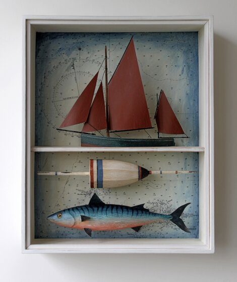 Shadow box with a model of a red sailboat, a fishing float, and a hand-painted fish, set against a nautical chart background.