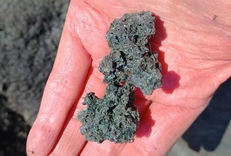 A person's hand holding a rough, dark-colored mineral sample with an irregular shape.