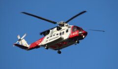 A red and white Coastguard helicopter in flight against a clear blue sky.