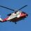 A red and white Coastguard helicopter in flight against a clear blue sky.