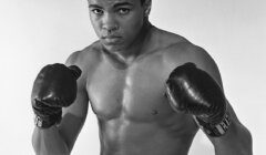 A black-and-white photo of an unidentified male boxer in a fighting stance, wearing boxing gloves and shorts.